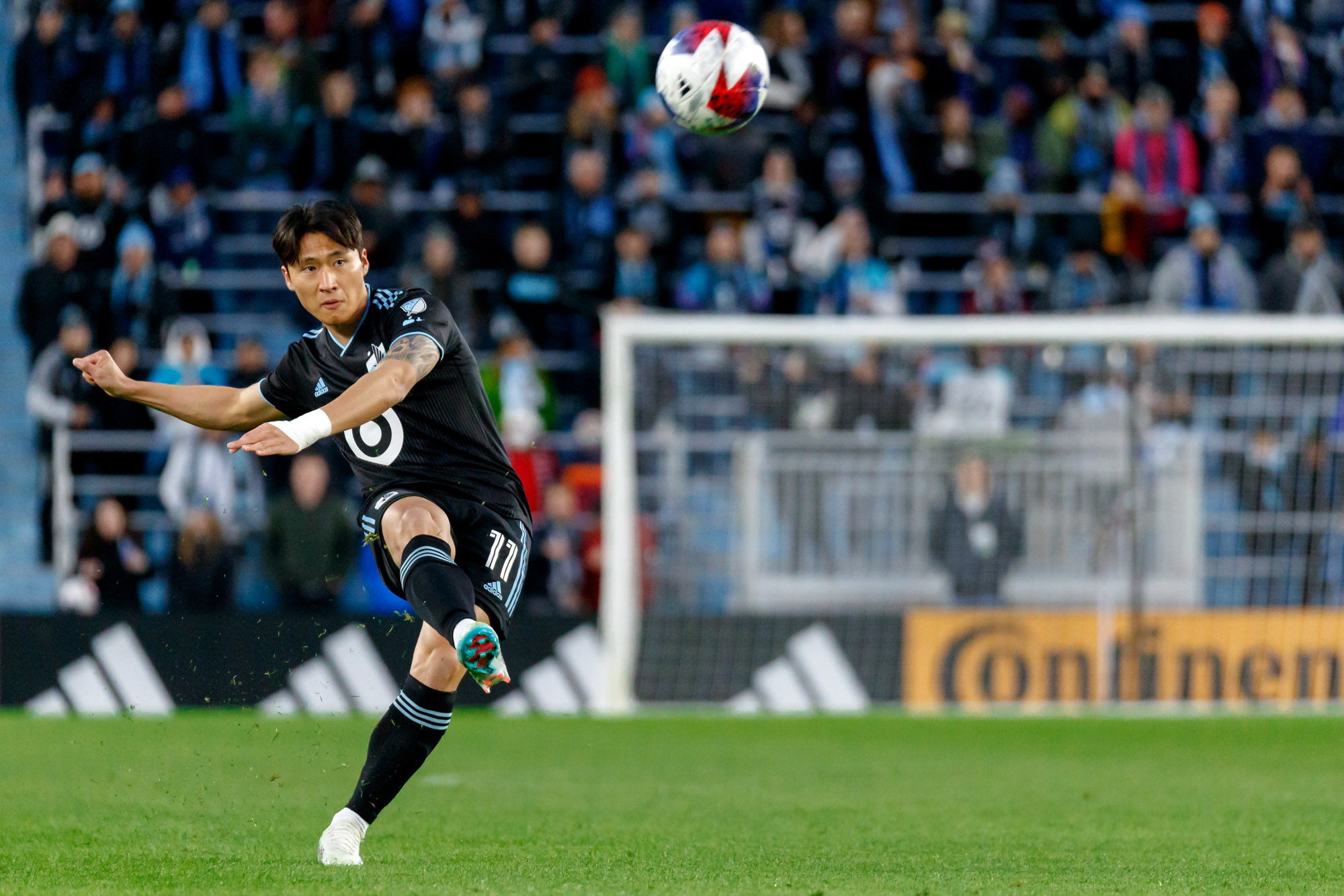 Sang Bin Jeong kicks the ball as blades of grass are flung into the air.