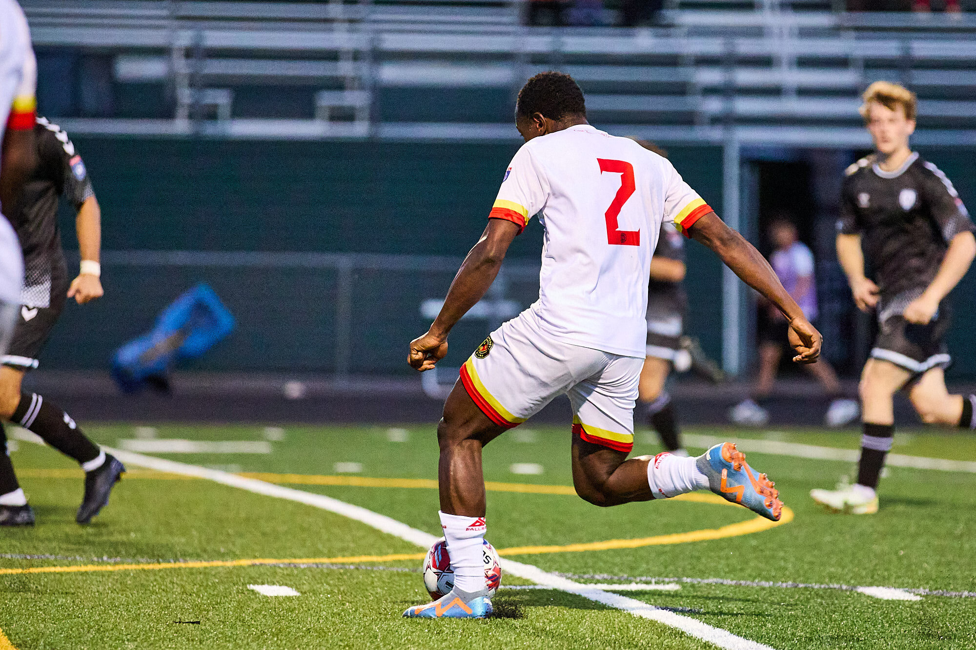 A soccer player wearing a red number 2 on a white kit lines up the ball, ready to strike. 