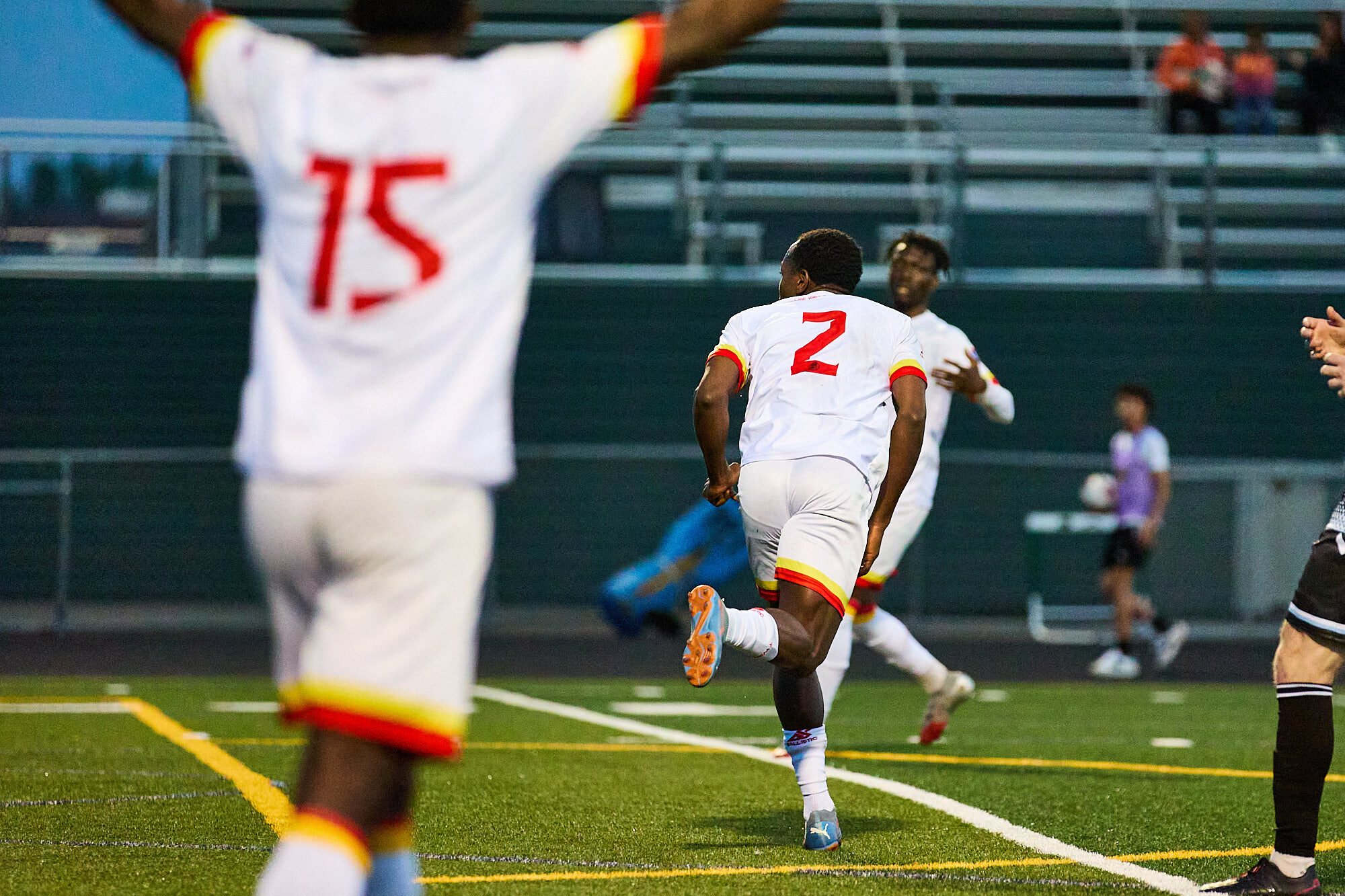 A blurred player wearing 15 is back-to-the-camera, hands aloft. A player with the number 2 on his back is partially turned . 
