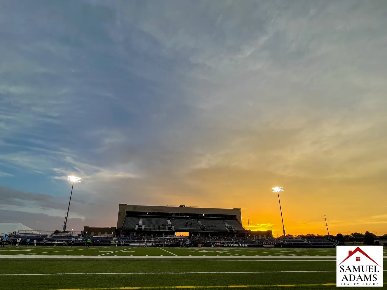 The sun sets behind a grandstand, with floodlights on either side