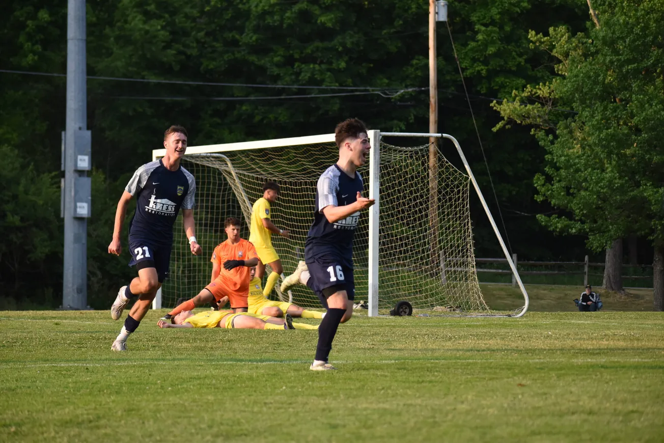 Five soccer players are pictured (left to right): A player in black jersey and shorts, one orange jerseyed player and one yel