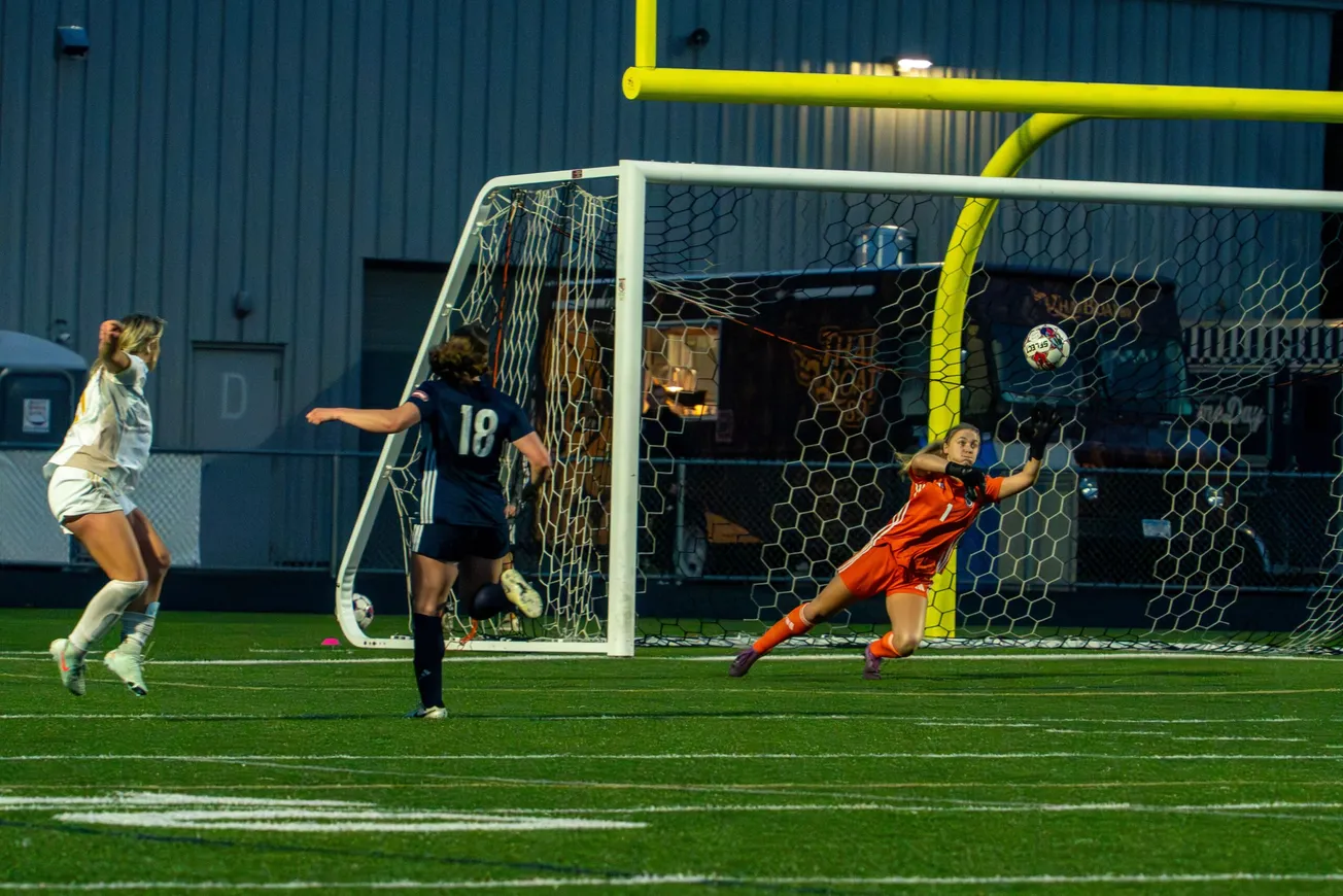 White shirted striker scores past a keeper in orange